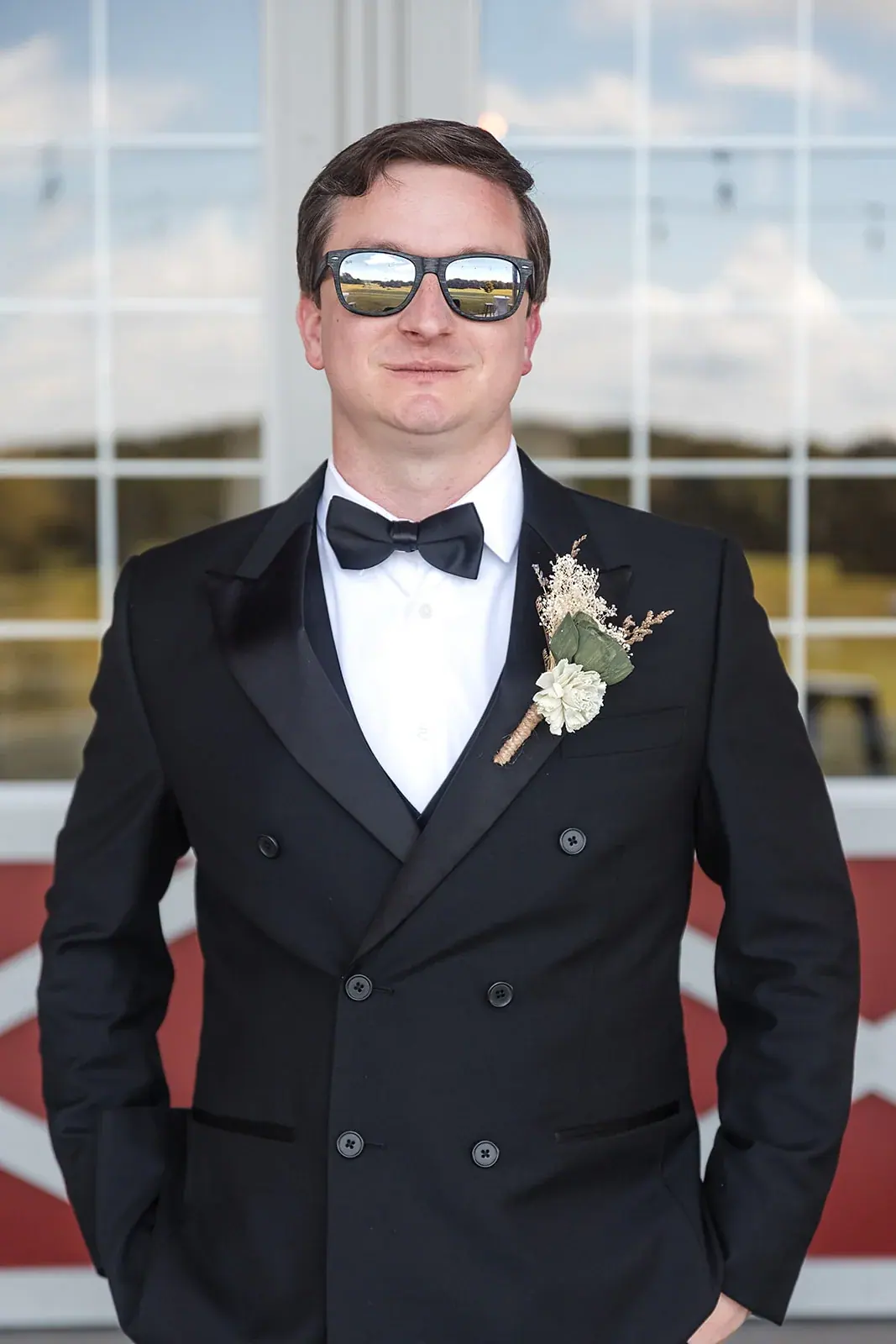 Groom in a black tuxedo and sunglasses outside the barn