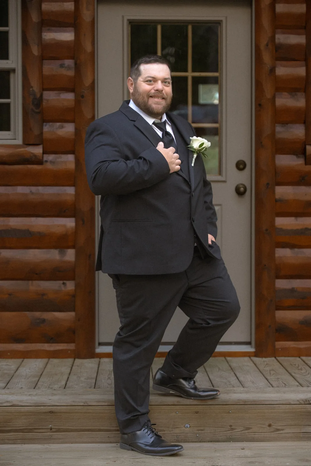 groom standing on cabin porch adjusting jacket, getting ready