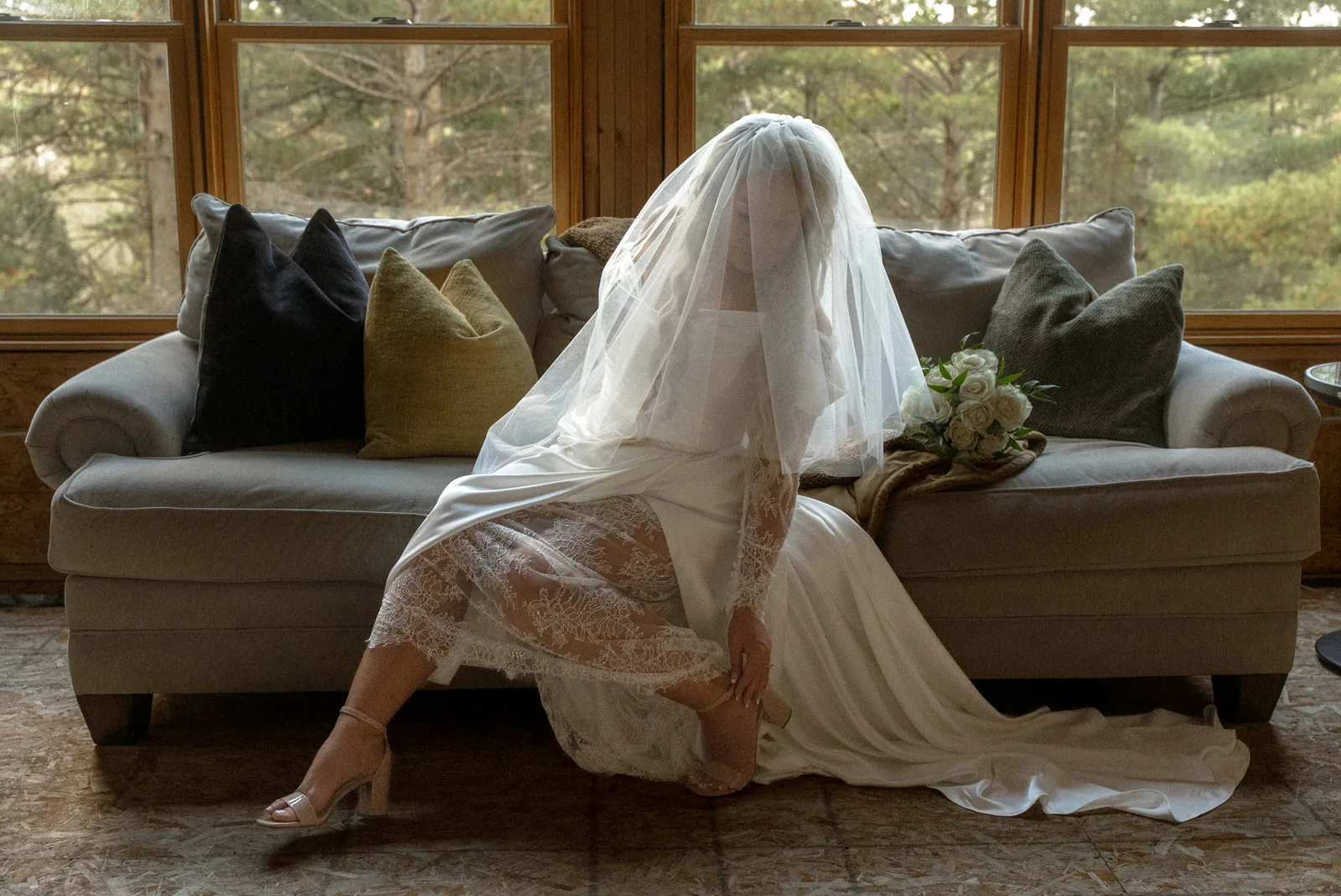 bride seated sideways on couch in sunroom with bouquet, color