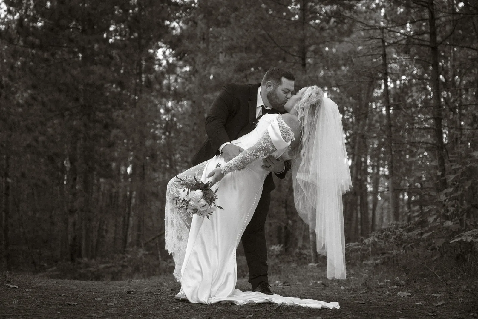 bw dip kiss portrait of bride and groom in woods