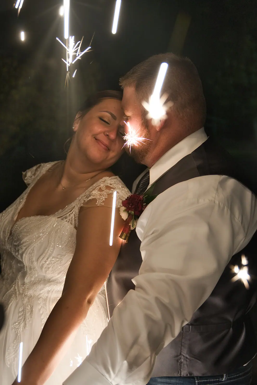 Couple cuddling close sparkler between them — Chelsea & Jake's wedding at Ogemaw County Fairgrounds, West Branch, MI
