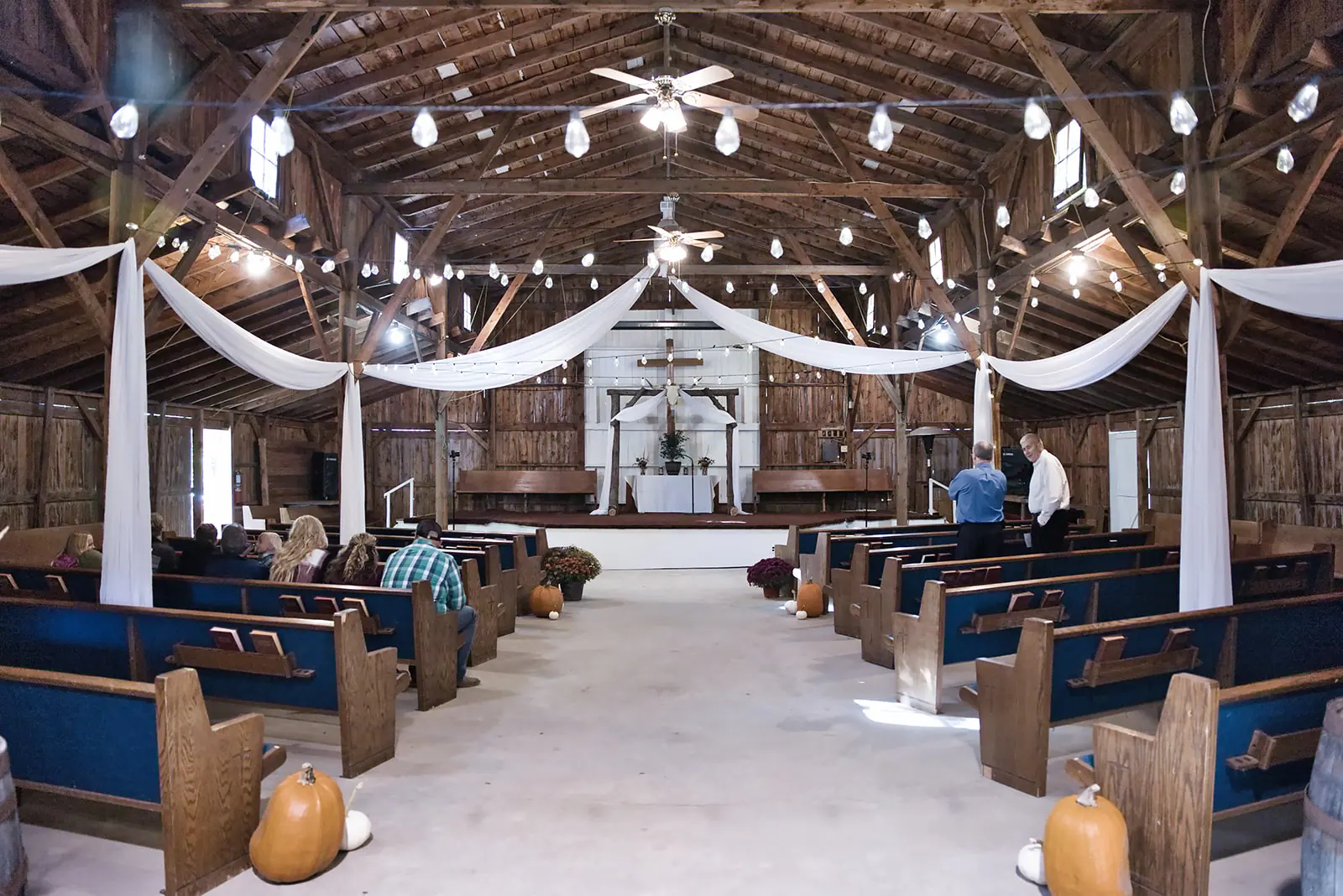 Wide barn interior pews white drapes — Chelsea & Jake's wedding at Ogemaw County Fairgrounds, West Branch, MI