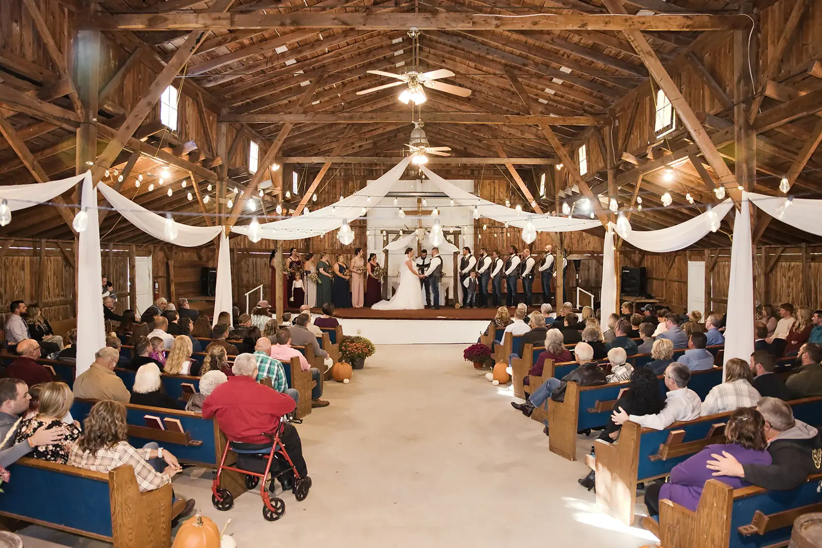 Wide shot barn ceremony guests seated — Chelsea & Jake's wedding at Ogemaw County Fairgrounds, West Branch, MI