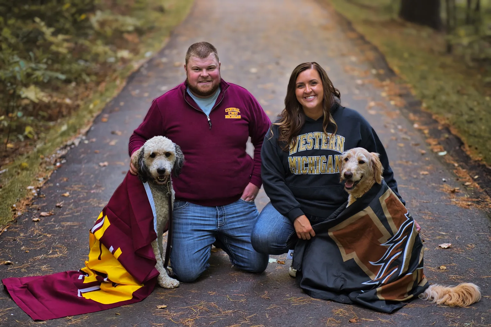 couple kneeling with two dogs, college sweatshirts and blanket
