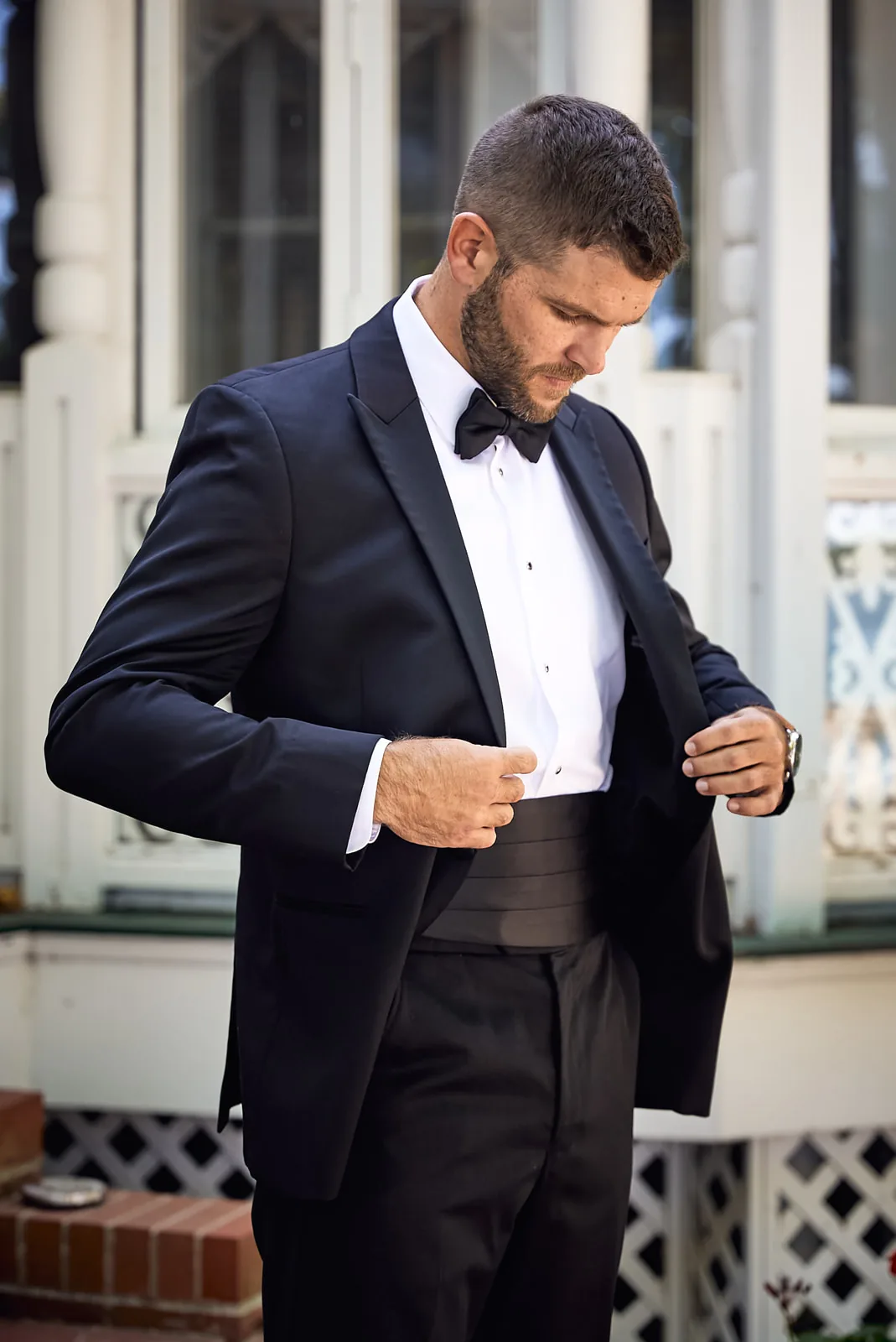 bw groom portrait adjusting cufflink on porch
