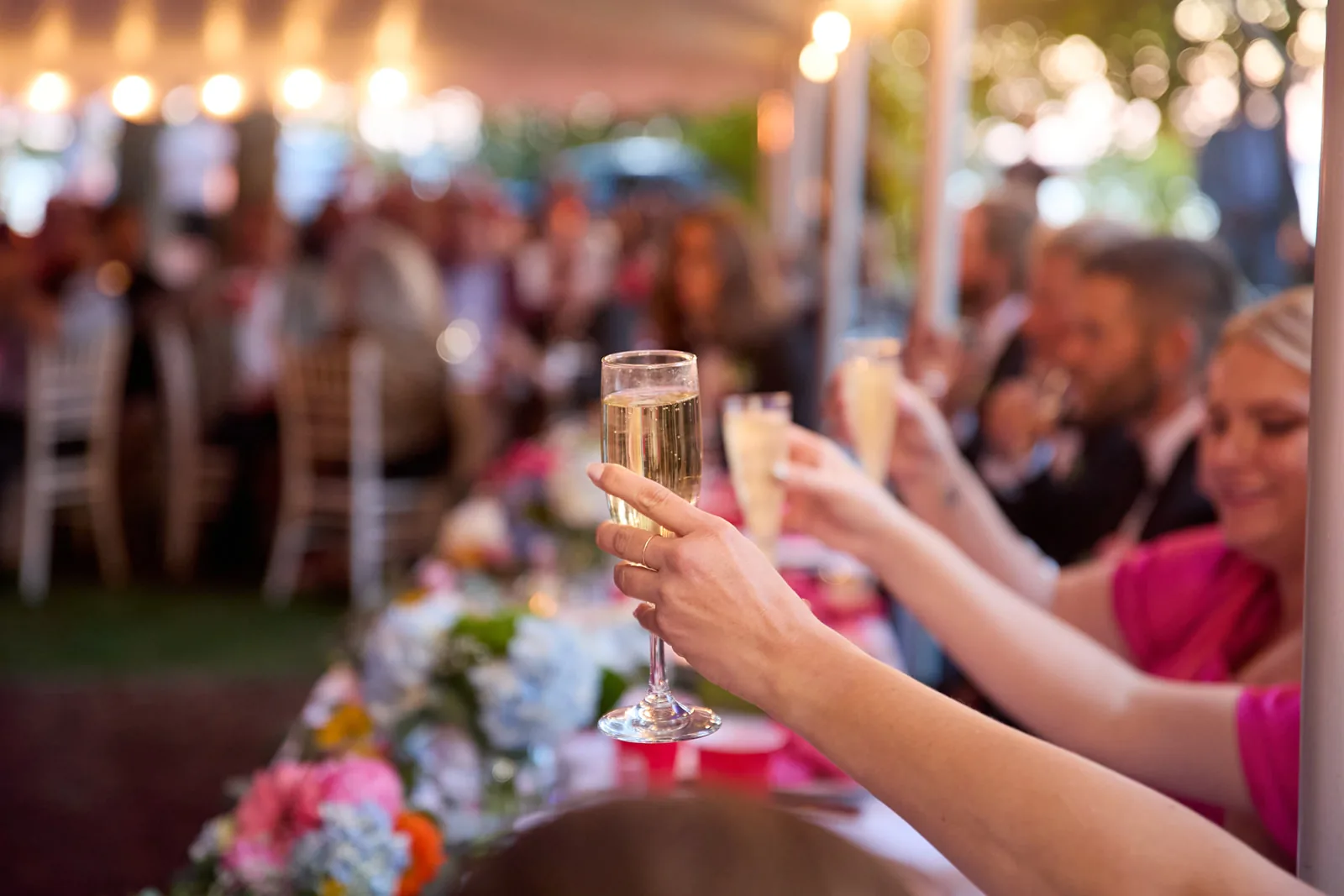 reception toast, guests raising champagne glasses under tent