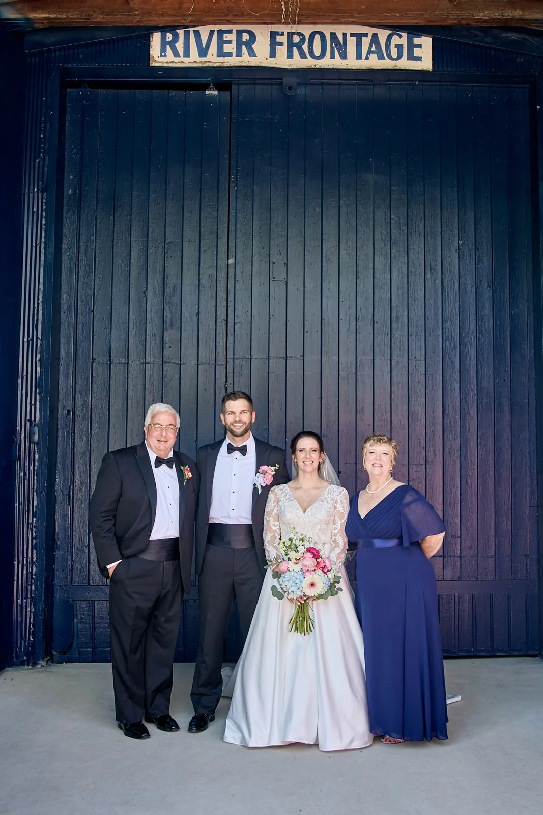 bride groom with parents group portrait, blue boathouse wall backdrop