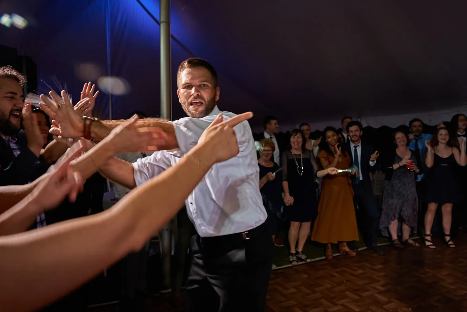 reception candid guests reaching hands forward dancing, tent lighting
