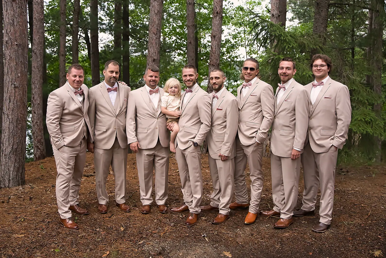 Groomsmen tan suits standing pines child — Erika & Corey's wedding at Sojourn Lakeside Resort, Gaylord, MI