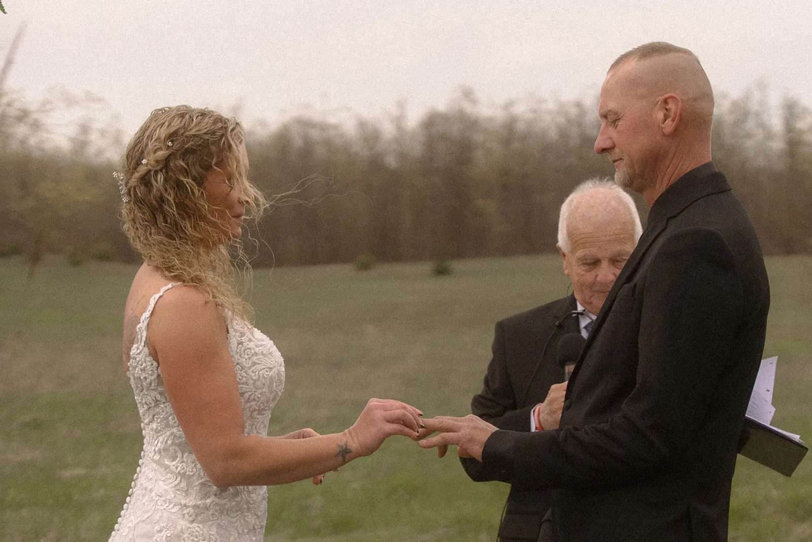 officiant placing ring on bride hand during ceremony, windy hair