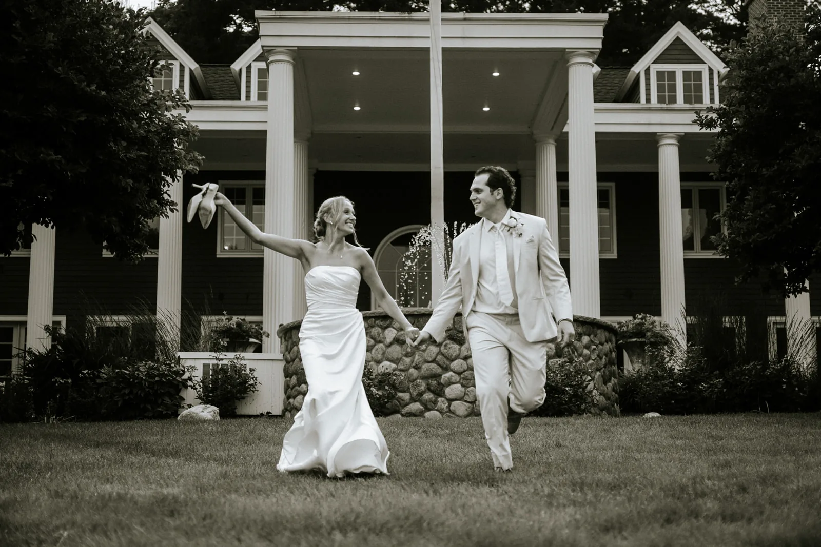 wide shot bride and groom running hand in hand in front of mansion porch