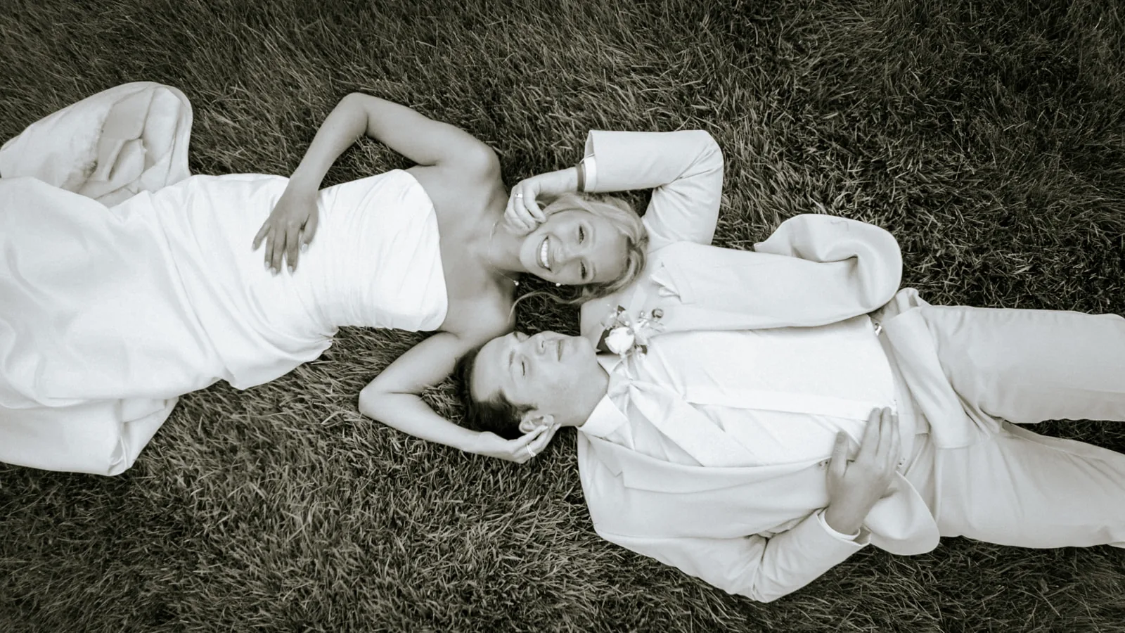 bw wide shot couple lying in grass together, playful pose