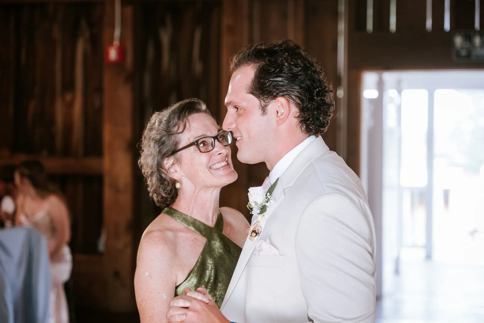 bride dancing with older guest, laughing, barn doorway light