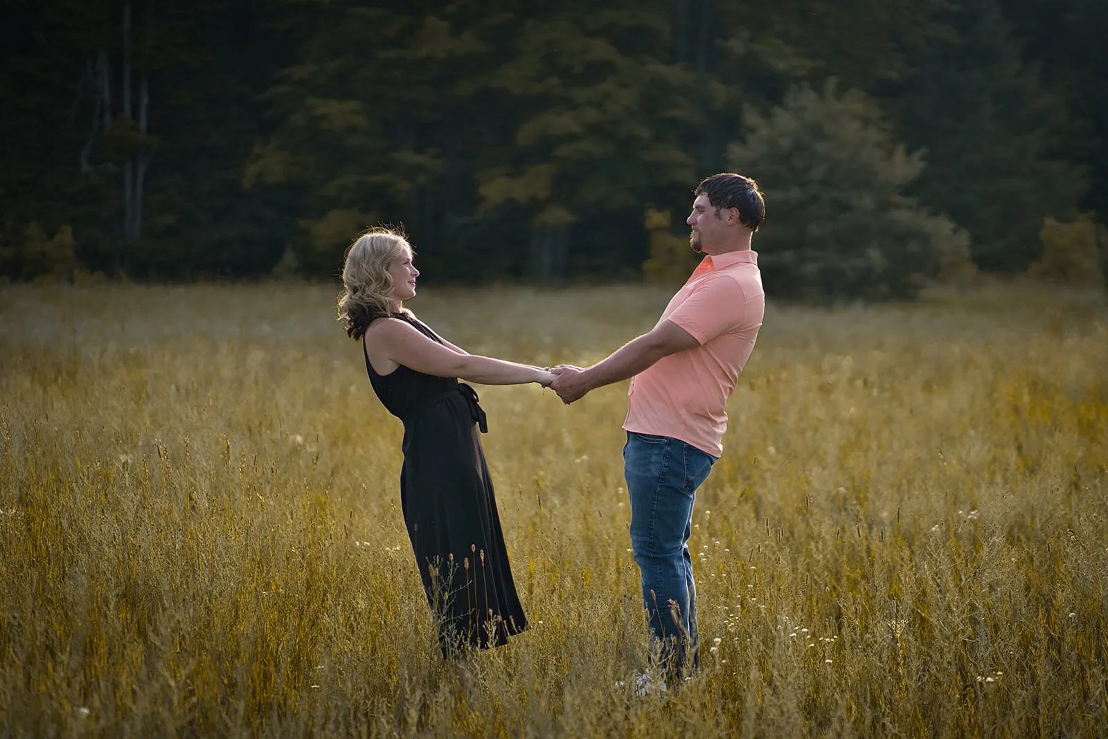 couple holding hands walking through golden grass field