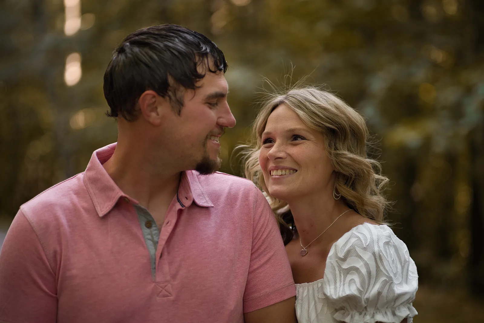 couple close portrait smiling, pink shirt, forest backdrop