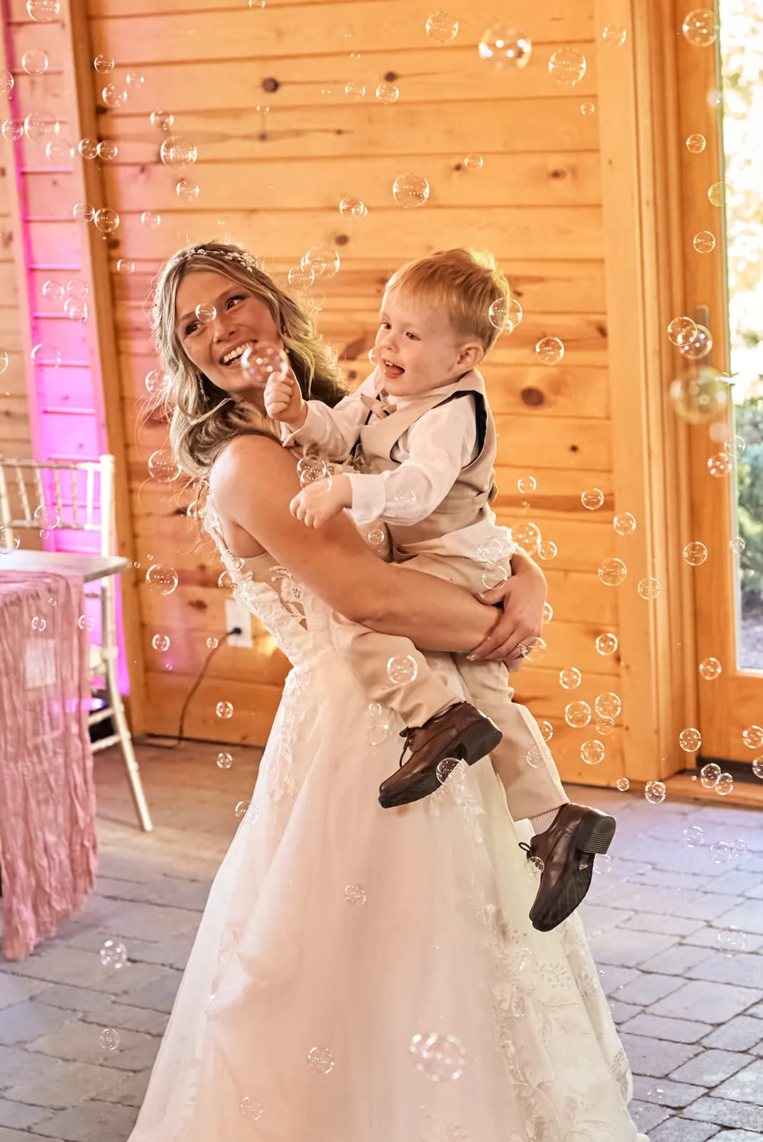bride holding young boy amid floating bubbles, candid reception