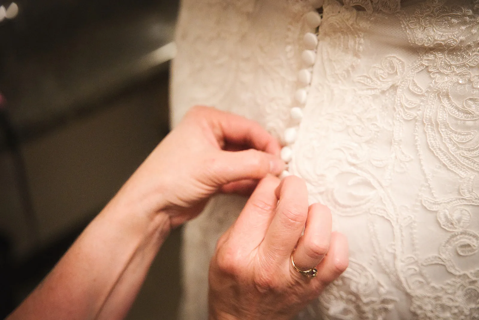 detail of hands buttoning back of wedding dress