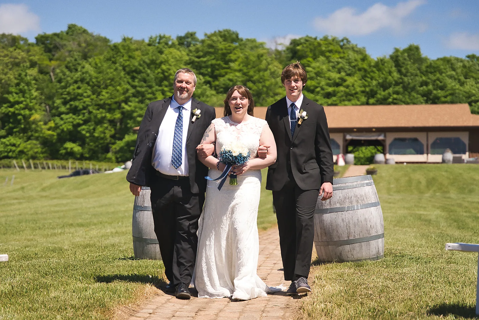 wide shot bride and groom walking brick aisle toward barn venue