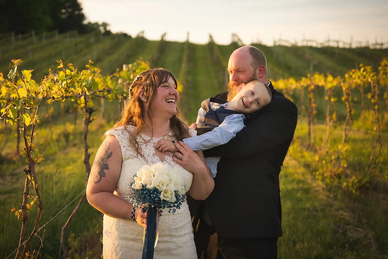 bride and groom with ring bearer boy, playful group portrait, golden hour
