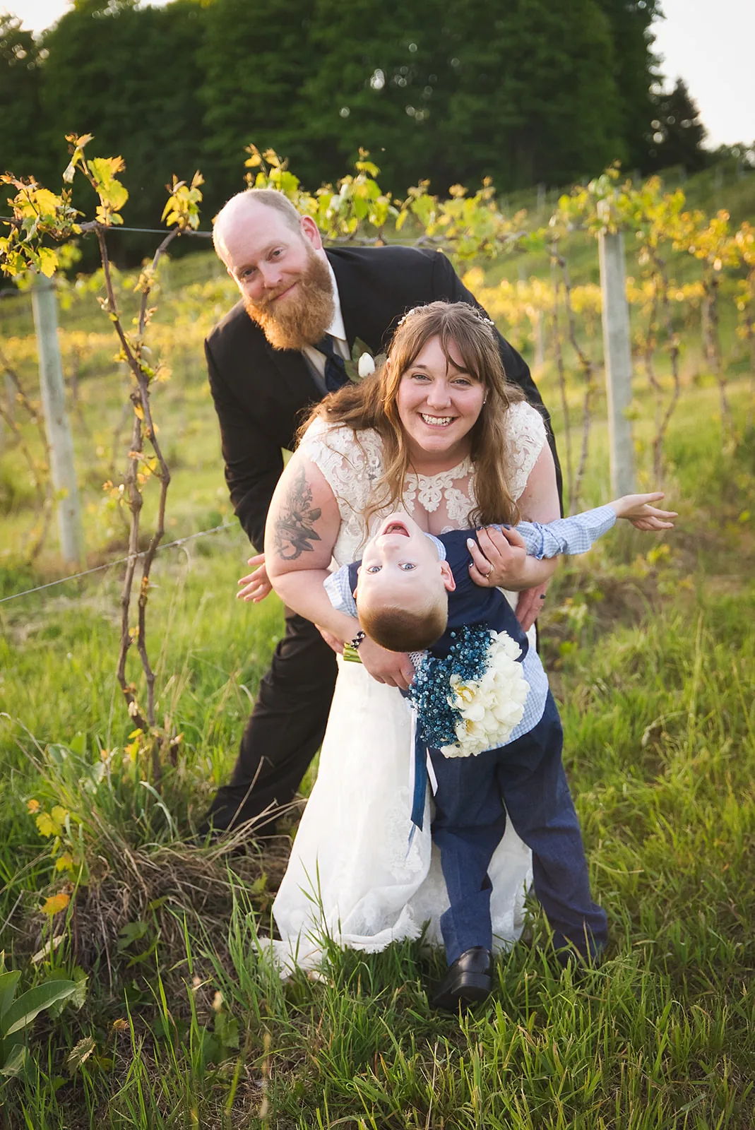 groom lifting ring bearer boy with bride, golden hour vineyard