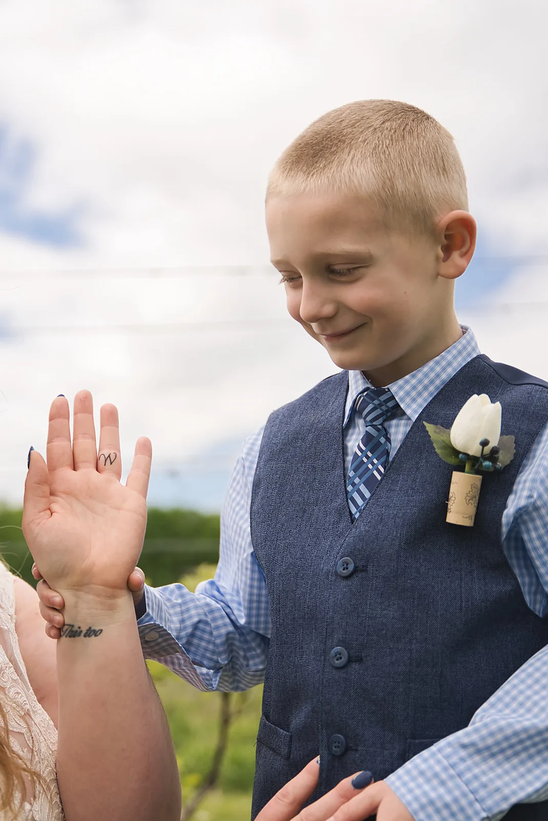 bride kneeling embracing ring bearer boy in vineyard field
