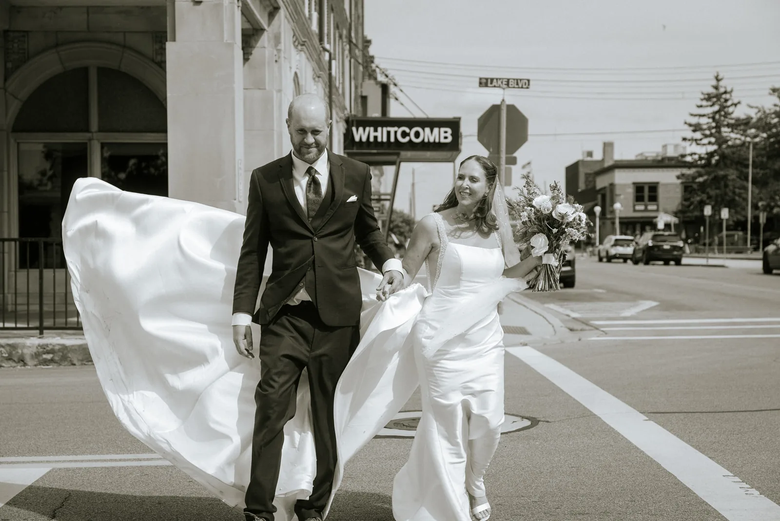 bw bride and groom walking through city crosswalk, different angle