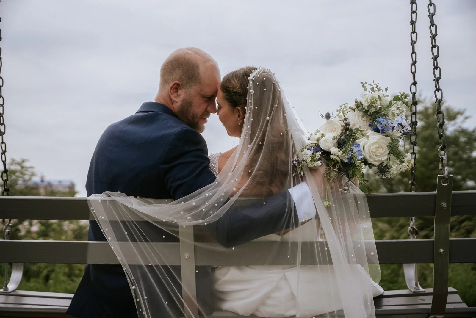 bw bride and groom embracing on porch swing, veil draped
