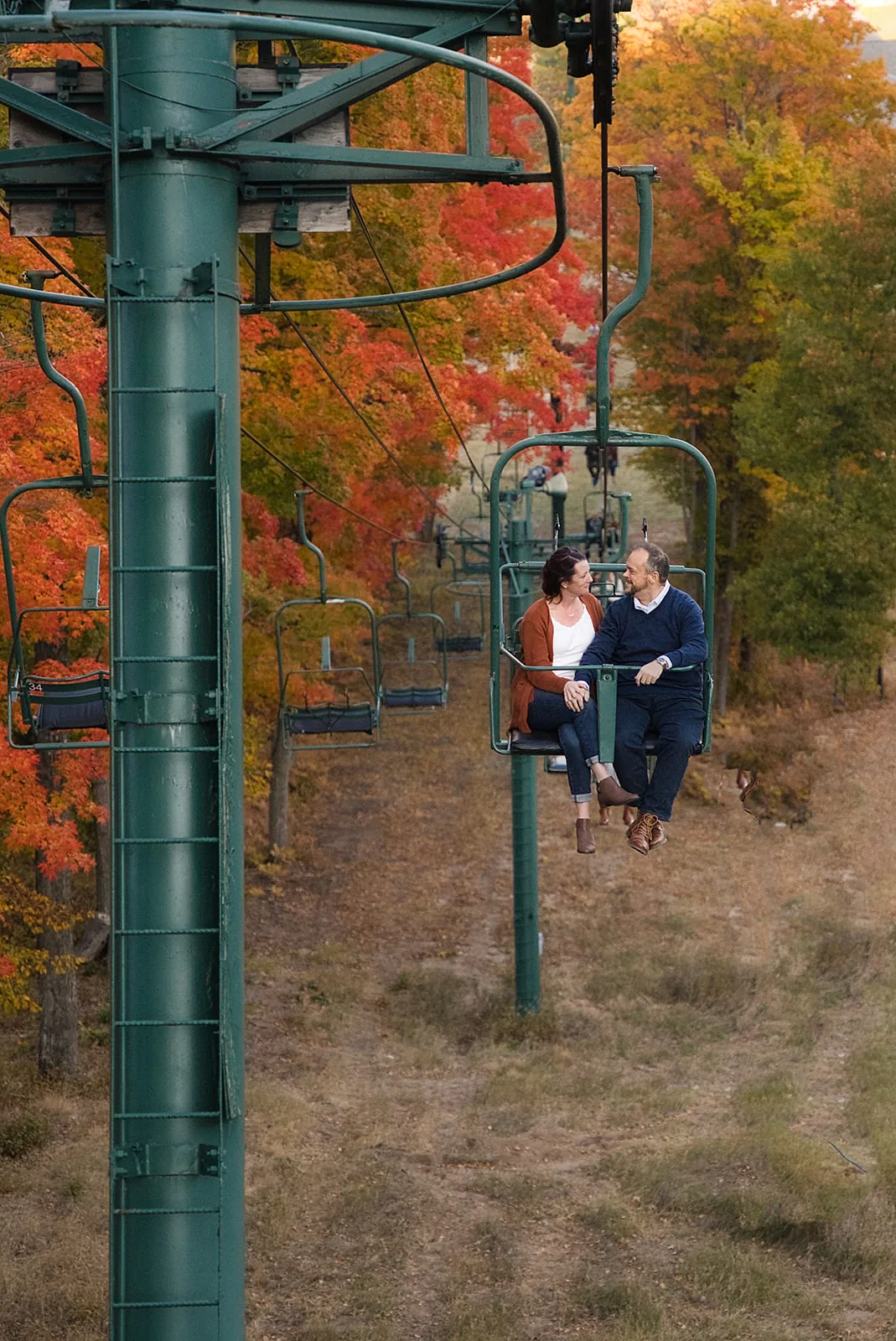 wide shot of couple riding ski chairlift through fall foliage