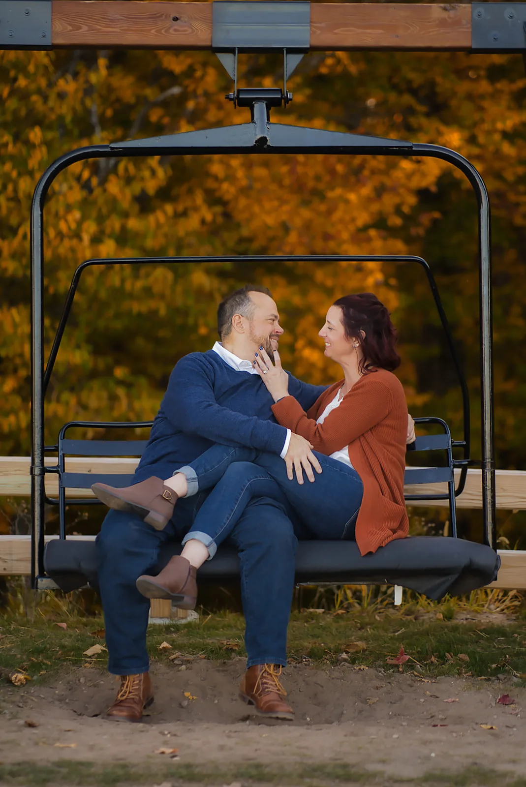couple nose-to-nose on chairlift bench, fall colors