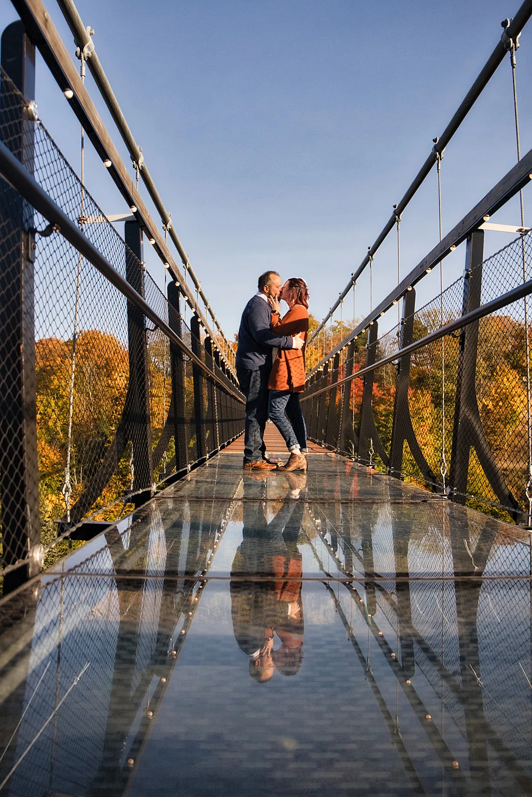 couple embracing on suspension bridge, wide shot with reflection