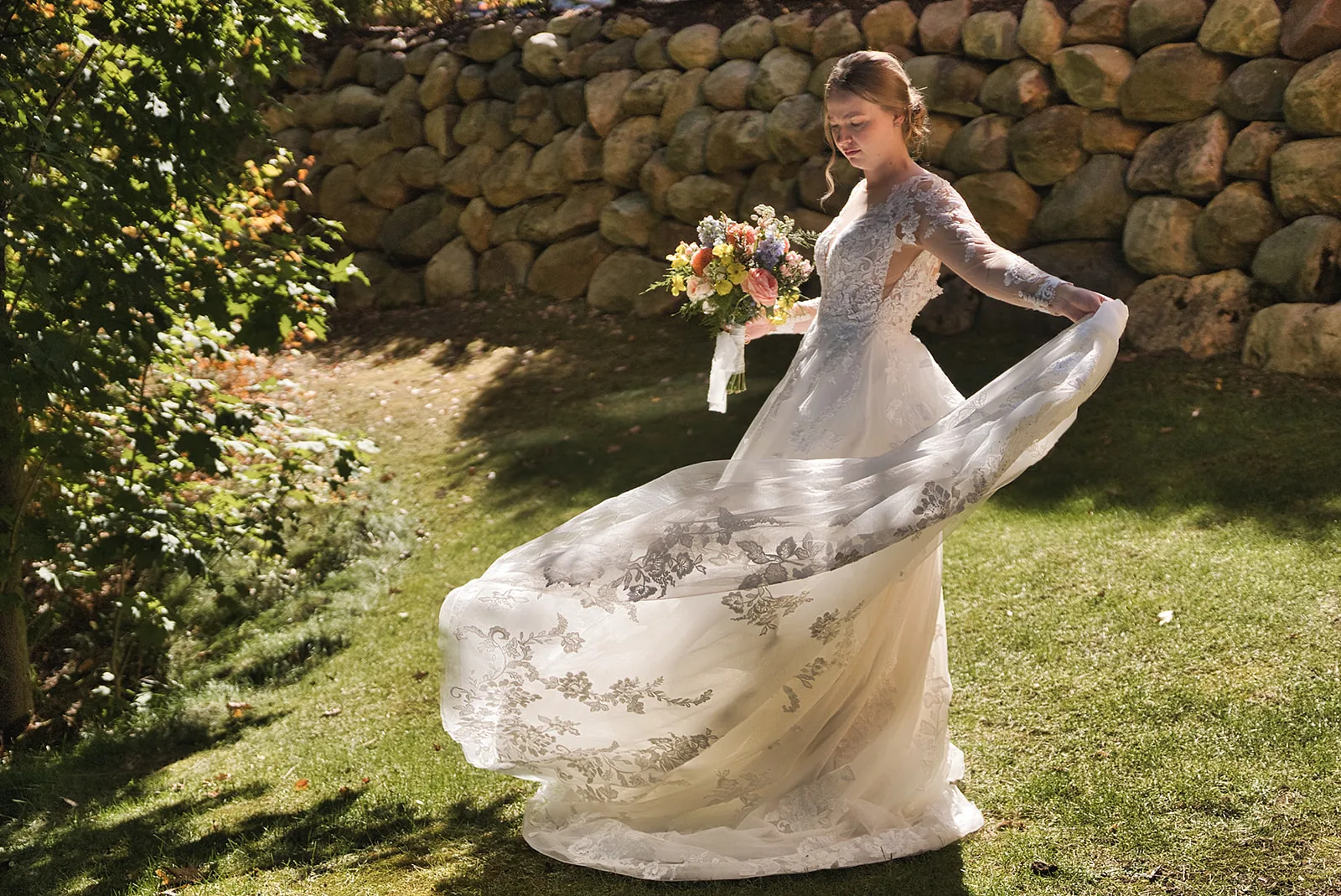 bride holding dress train, bouquet, stone wall backdrop