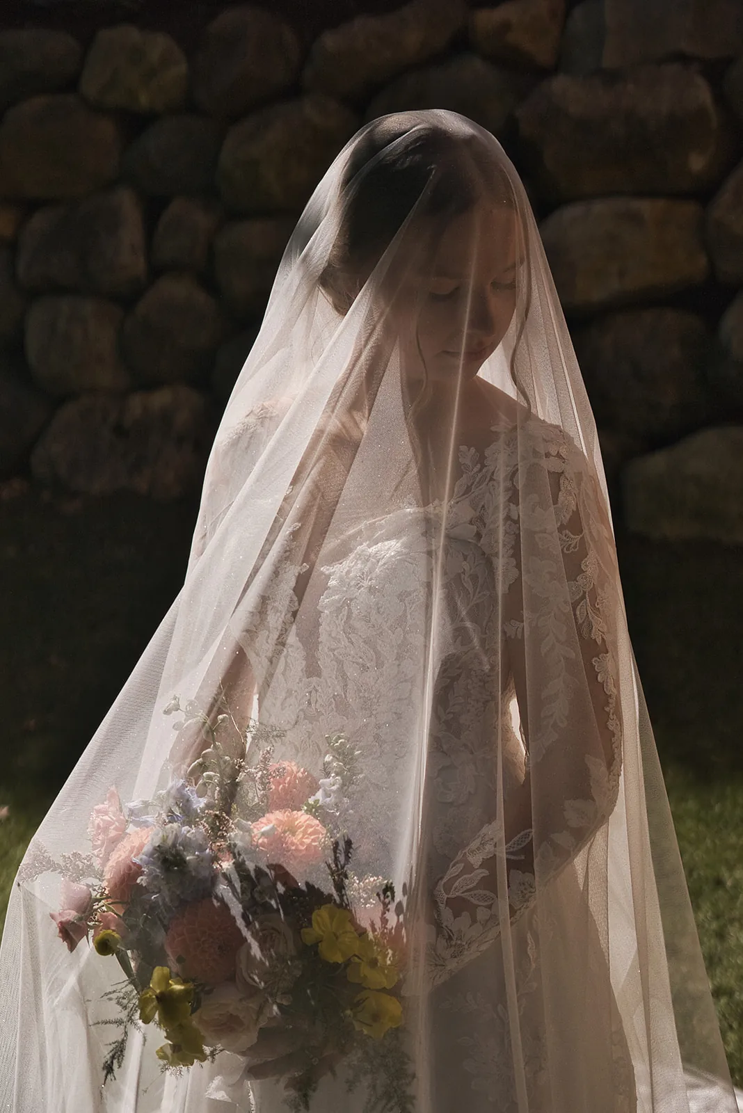 bride standing under long veil, bouquet, lawn setting
