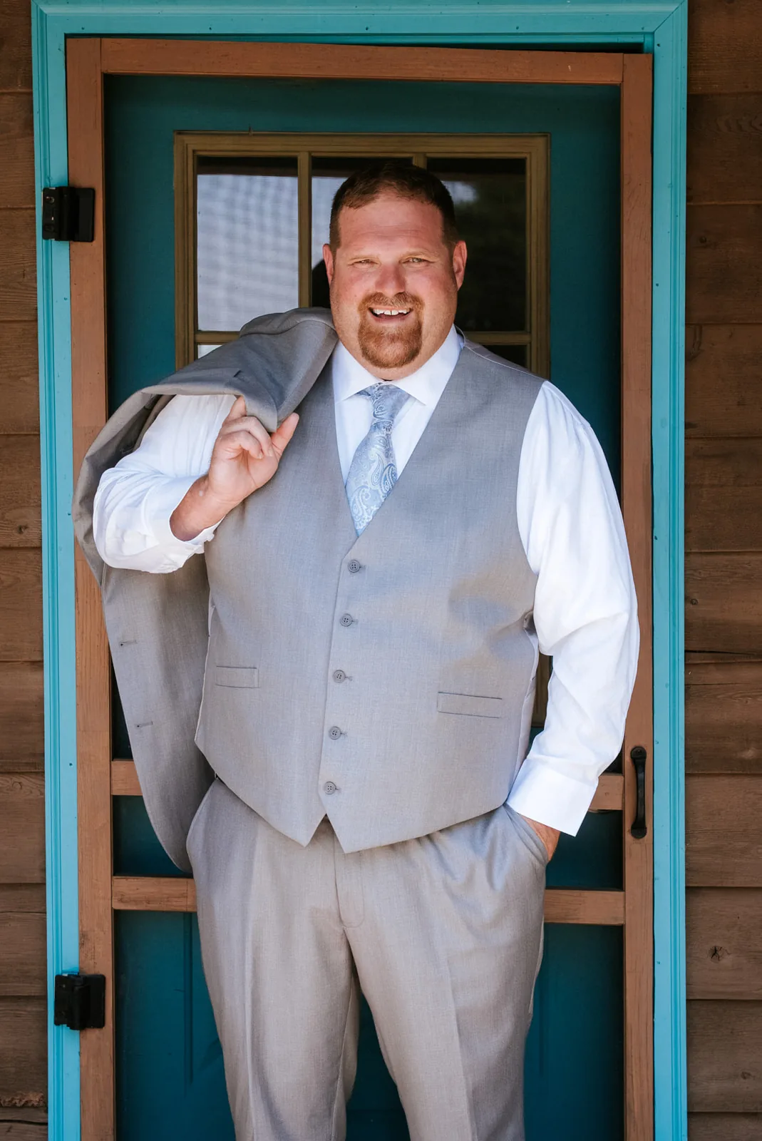 groom solo portrait at teal door, holding jacket over shoulder