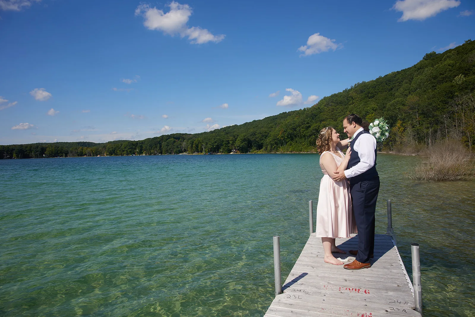 wide shot of bride and groom embracing on dock, lake water visible