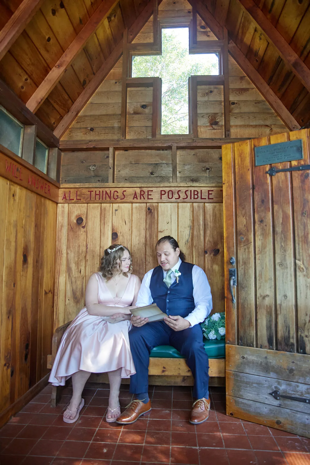bride and groom seated in chapel, "All Things Are Possible" door sign