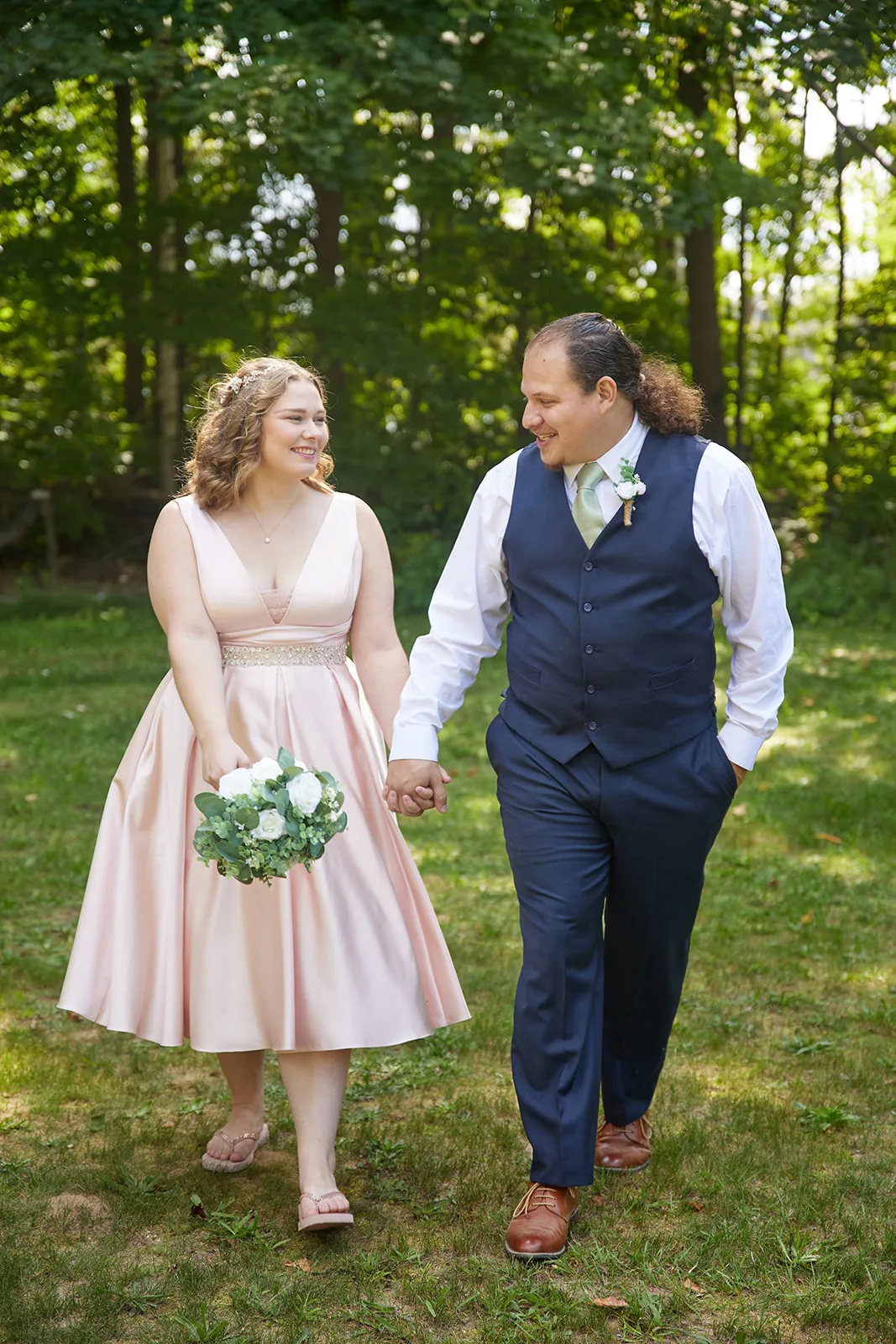 bride and groom walking hand in hand across lawn, candid