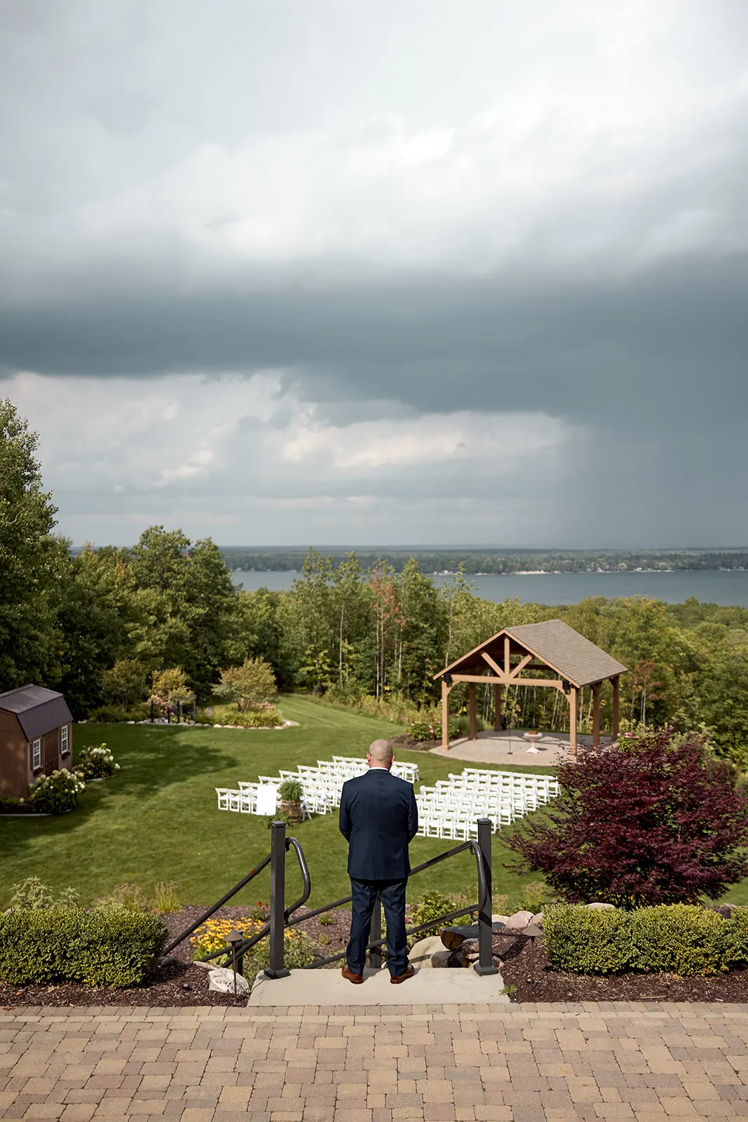 Groom standing alone lawn above lake — Taylor & Mark's wedding at The Manor at Fire Tower Hill, Lewiston, MI