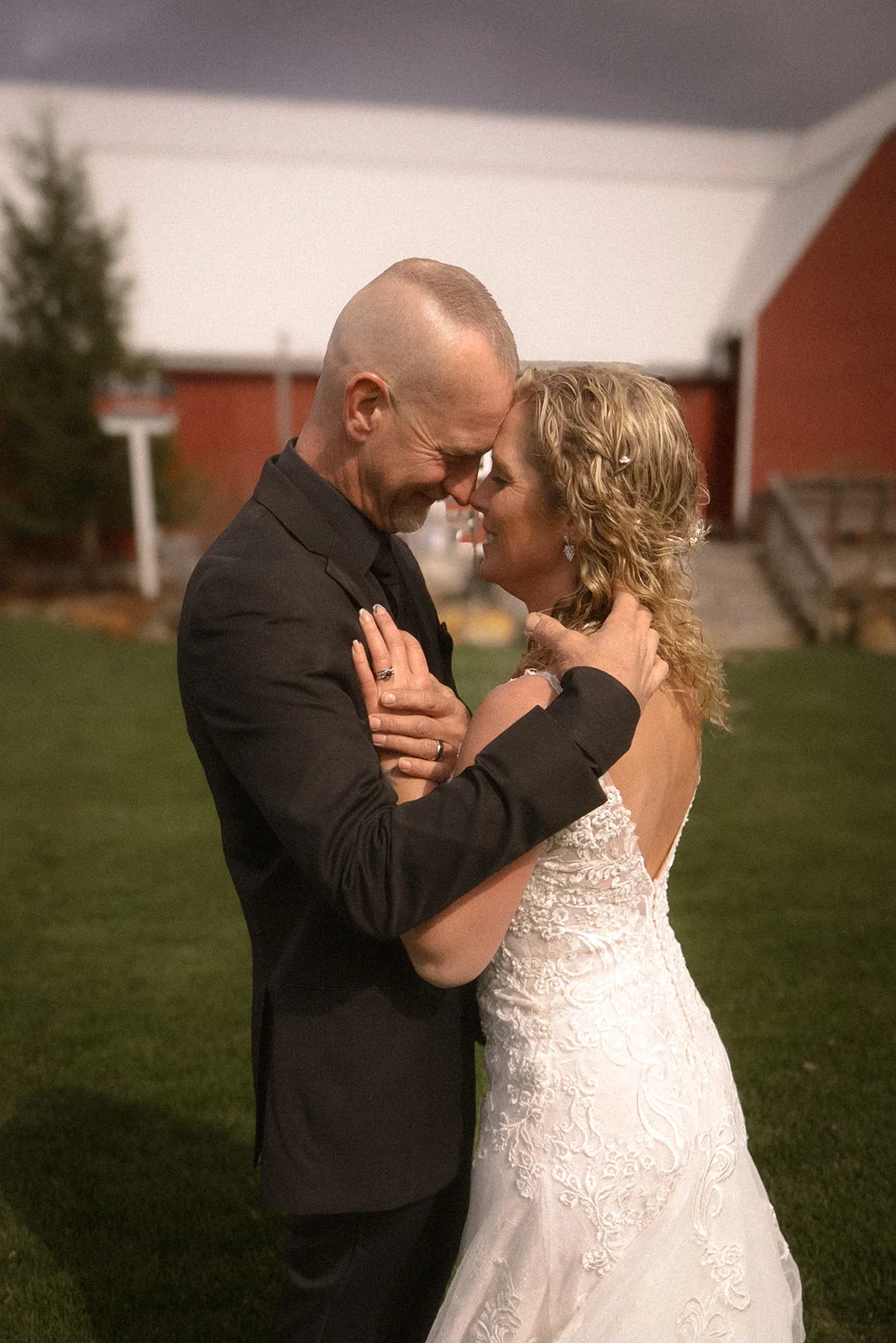 Warm, filmic portrait of a couple embracing forehead to forehead by a red barn