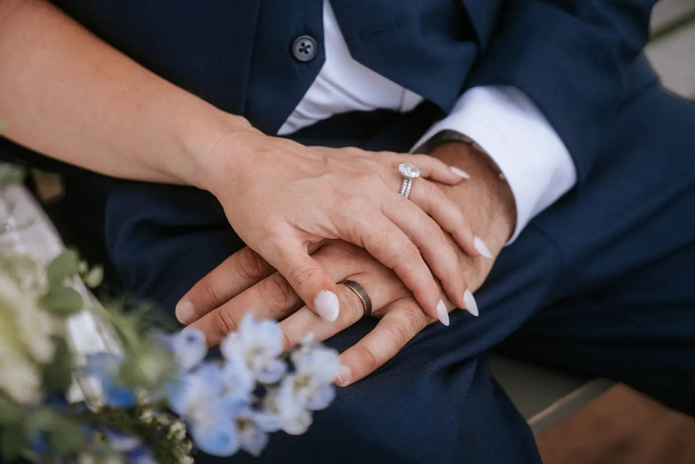 Close-up of clasped hands showing wedding and engagement rings